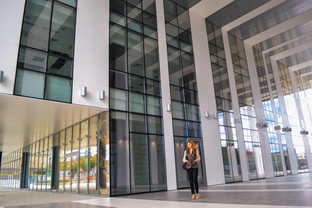 A fashionable woman in a modern glass lobby, showcasing urban architecture and style.